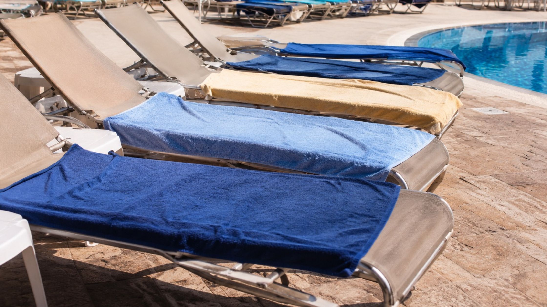 hotel guests reserving sunbeds with towels near swimming pool